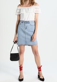 White off-the-shoulder blouse with lace trim, paired with a light blue denim skirt. Red ribbon-accents on black heels and a small black bag.