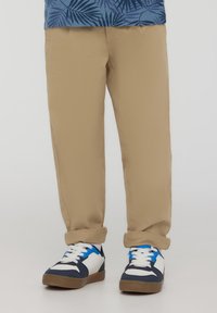 Pantaloni in cotone beige con risvolti, abbinati a sneakers bianche e blu con accenti blu e una suola texturizzata.