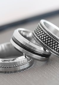 Vier metalen ringen op elkaar gestapeld, met verschillende texturen: een gevlochten band, een glad gepolijste oppervlakte en een met een gemusterde zwarte accenten.