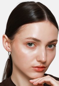 Orecchini pendenti in argento con design geometrico, caratterizzati da accenti di cristallo trasparente. Modella che li indossa con un outfit dalle tonalità neutre.