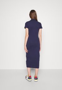 Námořnická modrá, přiléhavá polo šaty s krátkými rukávy a délkou po střed lýtek. V kombinaci s barevnými teniskami s různými akcenty.