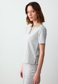 Korte mouw polo in lichtgrijs met een geometrisch patroon in crème en beige. Voorzien van een kraag en zijsplitten aan de onderkant.