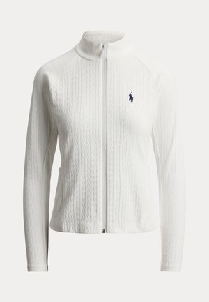 Balta adīta jaka ar rāvējslēdzēju, augstu apkakli, garām piedurknēm, smalku pinuma rakstu un nelielu tumši zilu izšūtu logotipu kreisajā krūtīs.