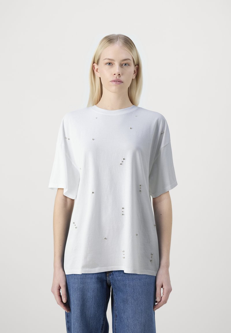 Camiseta blanca de corte oversized hecha de algodón, con adornos dispersos. Mangas cortas y diseño de cuello redondo. Sencilla y texturizada.