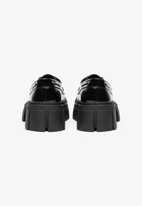 Črne lakirane čevlje z debelim podplatom. Gladka tekstura z zaobljenim nosom in dekorativnimi detajli na zgornjem delu. Oblikovani za dolgo življenjsko dobo.