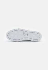 Semelle de sneaker blanche en caoutchouc avec un motif de semelle en chevrons, présentant un logo central embossé dans un style minimaliste. Texture lisse dans l'ensemble.