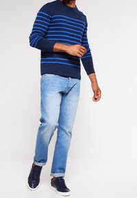Marineblauer gestreifter Pullover mit hellblauen horizontalen Streifen, kombiniert mit hellblauen Jeans und dunklen Sneakers. Lässiger Schnitt und bequeme Passform.