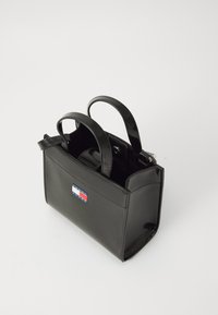Sac à main en cuir verni noir avec un design structuré, deux poignées supérieures et un patch logo à l'avant comportant des rayures rouges, blanches et bleues.