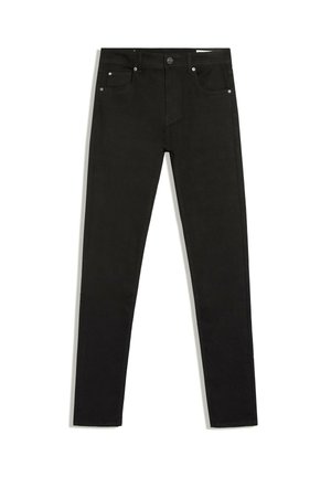 Gros plan d'une personne portant un jean noir taille haute avec des poches arrière et un top gris court à manches longues, mains dans les poches avant.