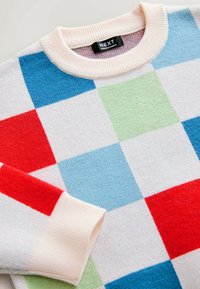 Farebný, nadrozmerný sveter s dizajnom patchwork s červenými, modrými, zelenými a bielymi štvorcami. Rebrovaný krémový golier a manžety. Mäkká textúra.