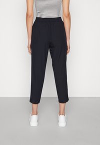 Černé zkrácené kalhoty s elastickým pasem, s hladkým povrchem a bočními kapsami, spárované s bílými teniskami.