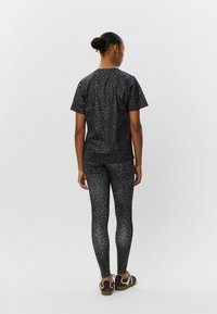 Čierny tričko s leopardím vzorom a legíny; mäkká, elastická látka; krátke rukávy; priliehavý strih; skombinované s hnedými teniskami a jednoduchým účesom.