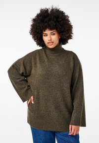 Oliveowy, oversize sweter z golfem w miękkim, teksturowanym splocie. Posiada prążkowane mankiety i dół, co zapewnia luźny krój. W połączeniu z niebieskimi dżinsami.