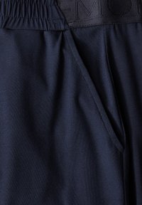 Navy blue juoksuhousut, joissa on sileä sävy ja elastinen vyötärö. Pidetty sivutasku ja brodeerattu brändäys vyötäröllä.