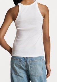 Vit ribbad tanktop med rund halsringning, slim fit och lätt sprund på sidan, kombinerad med ljusblå denimjeans med bakfickor.