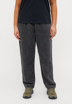 Dark gray baggy jeans with a faded texture and elastic cuffs, paired with olive green athletic shoes and a black t-shirt.