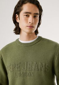 Žalia megzta palaidinė su apvalia kaklo iškirpte ir tekstūruota raštais. "Pepe Jeans London" subtiliai išsiuvinėta priekyje.