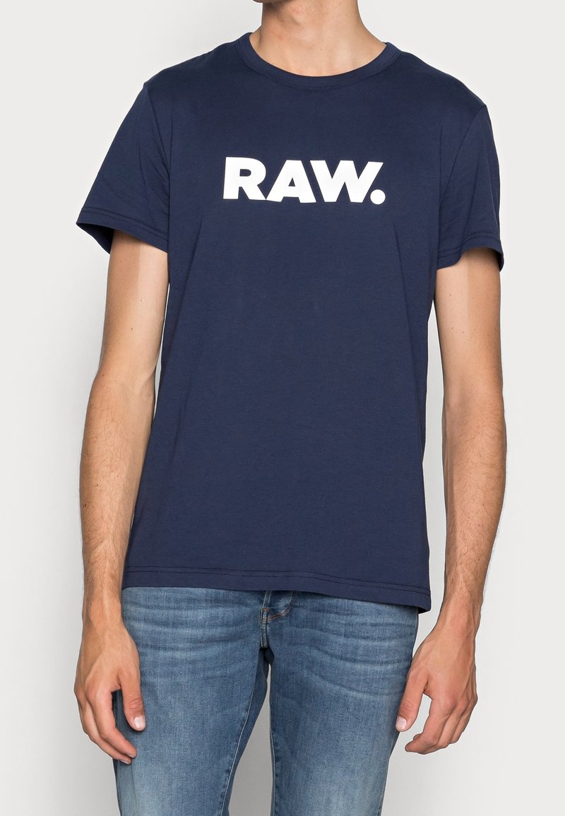 Náměsíčná modrá bavlněná tričko s krátkým rukávem, se výrazným bílým logem "RAW." na přední straně. Hladká textura, standardní střih.