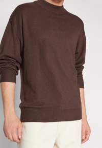 Brązowy sweter dzianinowy z kołnierzem typu mock, prążkowanymi mankietami i dołem. Miękka tekstura, luźny krój i opadające ramiona. Idealny na codzienne stylizacje.