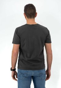 T-shirt grigio scuro a maniche corte con colletto girocollo, realizzato in tessuto morbido, abbinato a jeans in denim blu con un motivo cucito sulle tasche.