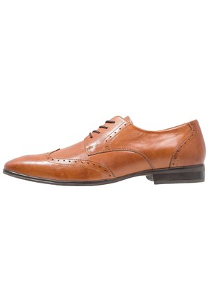 Zapato de vestir de cuero color marrón claro con un diseño elegante, punta afilada, detalles de brogue y cinco ojales para los cordones. Suela plana negra.