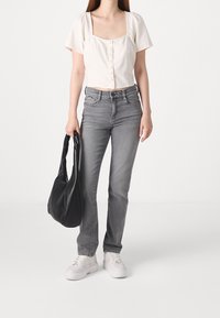 Top cropped bianco a maniche corte con bottoni, jeans grigi attillati, sneakers bianche con piattaforma e una borsa a tracolla nera. Design semplice e moderno.