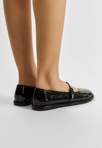 Zwarte gepatineerde leren ballerina's met een afgeronde neus, een klein strikje als accent en een slanke zwarte zool, die een gladde en glanzende oppervlakte tonen.