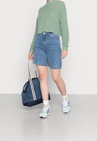 Ljust grön kortärmad tröja, blå denimshorts med trasig nederkant, vita strumpor, pastellfärgade sneakers och en blå toteväska med randiga handtag.