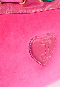 Borsa a tracolla in suede rosa con un dettaglio a forma di cuore in pelle testurizzata, recante la lettera "J" e cuciture bianche. Sono visibili dei dettagli in hardware oro.