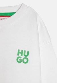 Weißer Sweatshirt mit geripptem Kragen und grünem, erhabenem "HU GO"-Logo auf der linken Brust. Weiches Material mit glatter Textur.