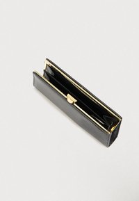 Musta teksturoidusta nahasta valmistettu lompakko, jossa on kultainen metallikehys ja lukko, avoinna ja näyttää tyhjät lokeroita vaalealla yksinkertaisella taustalla.