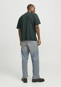 Camiseta de manga corta verde oscuro con un ajuste relajado y cuello redondo, combinada con jeans de mezclilla azul claro y zapatos negros.
