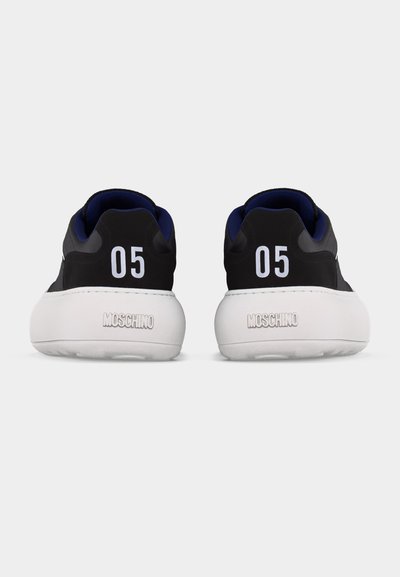 Poros juodų sportbačių su storais baltais padais, ant kulno apykaklės spausdinamas „05“, o ant užpakalinio pado įspaustas užrašas „MOSCHINO“.