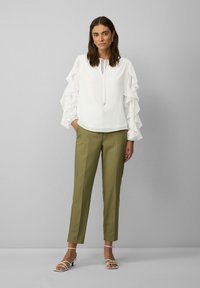 Blouse blanche avec des manches volantes, associée à un pantalon taillé vert olive et des sandales à lanières blanches. Design simple avec une coupe décontractée.
