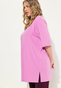 Rosa, kurzärmliges T-Shirt mit lockerer Passform, seitlichen Schlitzen und einer glatten Textur. Das Design ist einfach und unverziert.