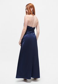Navy satin pitkä lattiapituinen mekko, jossa on istuva yläosa, kerätty yksityiskohta takana ja sileä, kiiltävä rakenne.