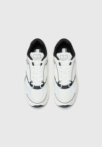 White athletic shoes with black accents. Features mesh and synthetic materials, structured design, prominent stitching, and laces.