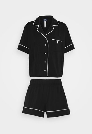 Zwart pyjama set bestaande uit een kortemouwen overhemd met knopen, een borstzak en witte piping, gecombineerd met shorts met elastische tailleband.