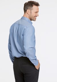 Ljusblå skjorta med knappar, texturerad krage och långa ärmar, i kombination med svarta byxor. Bakvyn framhäver skjortans passform och design.