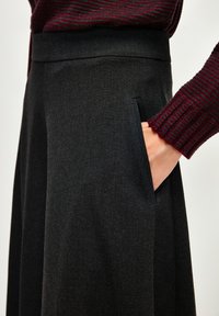 Pantaloni neri a vita alta realizzati in tessuto texturizzato, con una tasca laterale e una cintura liscia. L'outfit comprende un top borgogna a coste.