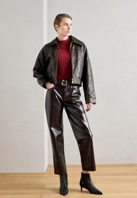 Zwarte leren cropped jack met een rood coltrui, glanzende donkerbruine broek en zwarte enkellaarsjes met hak. Simpel, op maat gemaakt ontwerp.