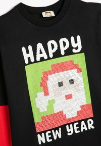 Schwarzes Baumwoll-T-Shirt mit einem Pixelkunst-Design von Santa und dem Text "FROHES NEUES JAHR" in Weiß, akzentuiert durch grüne und rote Blöcke.