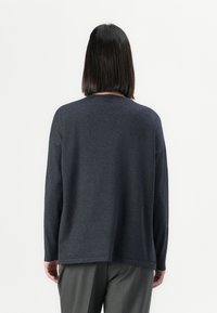 Maglione grigio scuro a maniche lunghe con vestibilità rilassata e scollatura rotonda. Tessuto morbido, orlo posteriore leggermente più lungo e cuciture delle spalle abbassate.