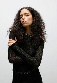 Zwarte kant lange mouwen top met een gestructureerde afwerking, met een ronde halslijn versierd met een zilveren kralenaccent. Zwarte high-waisted broek.