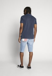 Polo blu navy a maniche corte, abbinata a pantaloncini di jeans azzurri con tasca applicata. L'outfit è completato da sneakers nere.