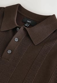 Bruine gebreide polo met een gestructureerde kraag, drie grijze knopen en verticale ribbelstructuur aan de voorkant. Merkenlabel zichtbaar aan de binnenkant.