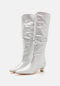 Bottes argentées montantes avec un design froncé, un bout pointu, un petit talon carré et une texture de surface scintillante.