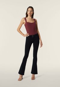 Body en bordeaux avec des bretelles larges, associé à un jean noir évasé. Le jean présente une fermeture à bouton et une légère texture. Fond clair.