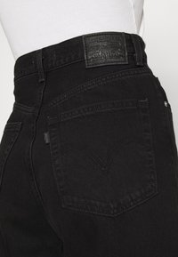 Vaqueros de mezclilla negra de cintura alta, con un bolsillo trasero cosido, parche de cuero de la marca Levi's y tejido texturizado.