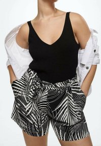 Zwarte geribbelde tanktop gecombineerd met zwart-witte shorts met bladerenpatroon, voorzien van een strik taille, zakken en een losse pasvorm. Witte blouse open gedragen.